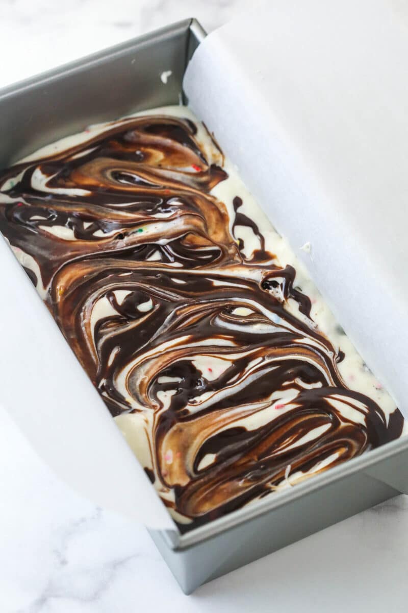 Swirling chocolate fudge sauce between layers of birthday cake ice cream.