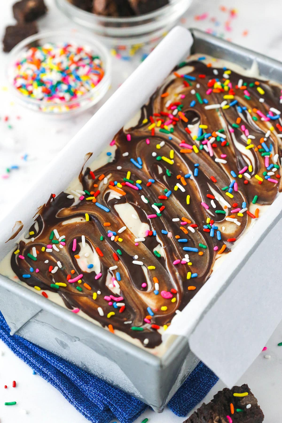Birthday cake ice cream in a loaf pan near a bowl of rainbow sprinkles.