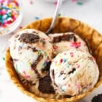 Scoops of birthday cake ice cream in a waffle cone bowl.