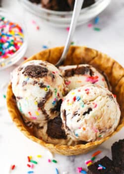 Scoops of birthday cake ice cream in a waffle cone bowl.