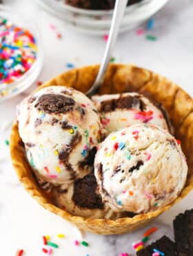 Scoops of birthday cake ice cream in a waffle cone bowl.