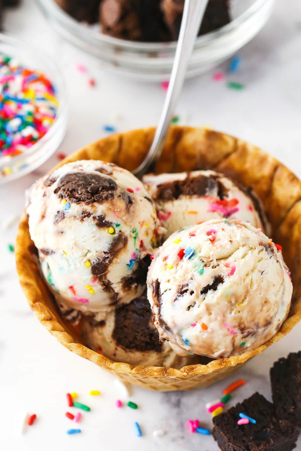 Scoops of birthday cake ice cream in a waffle cone bowl.