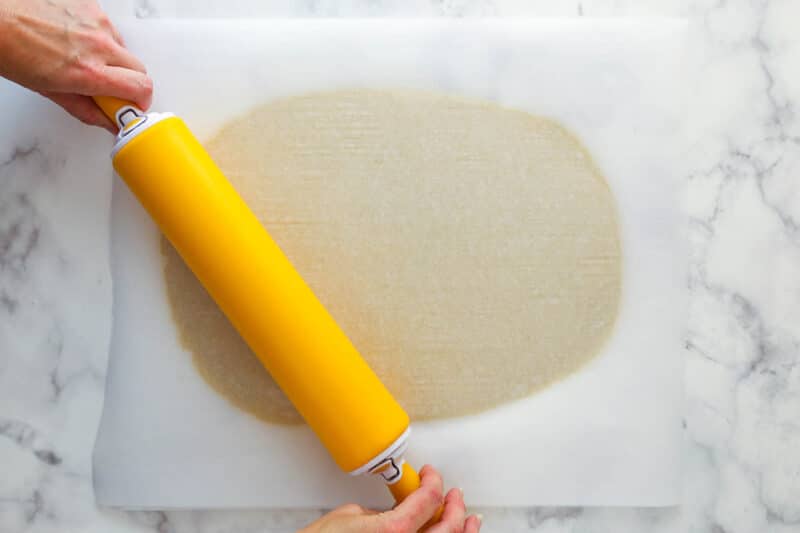 Rolling vanilla cookie dough flat between two layers of parchment paper.