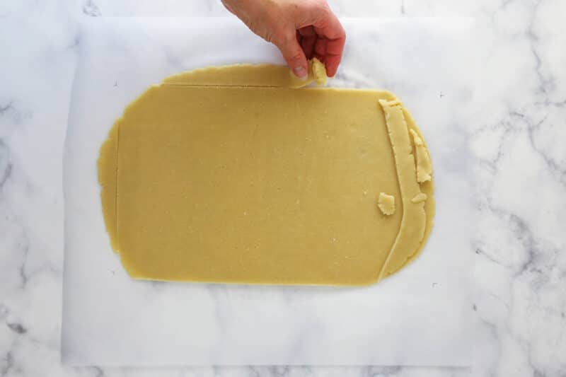 Removing rough edges from a rectangle of vanilla cookie dough.