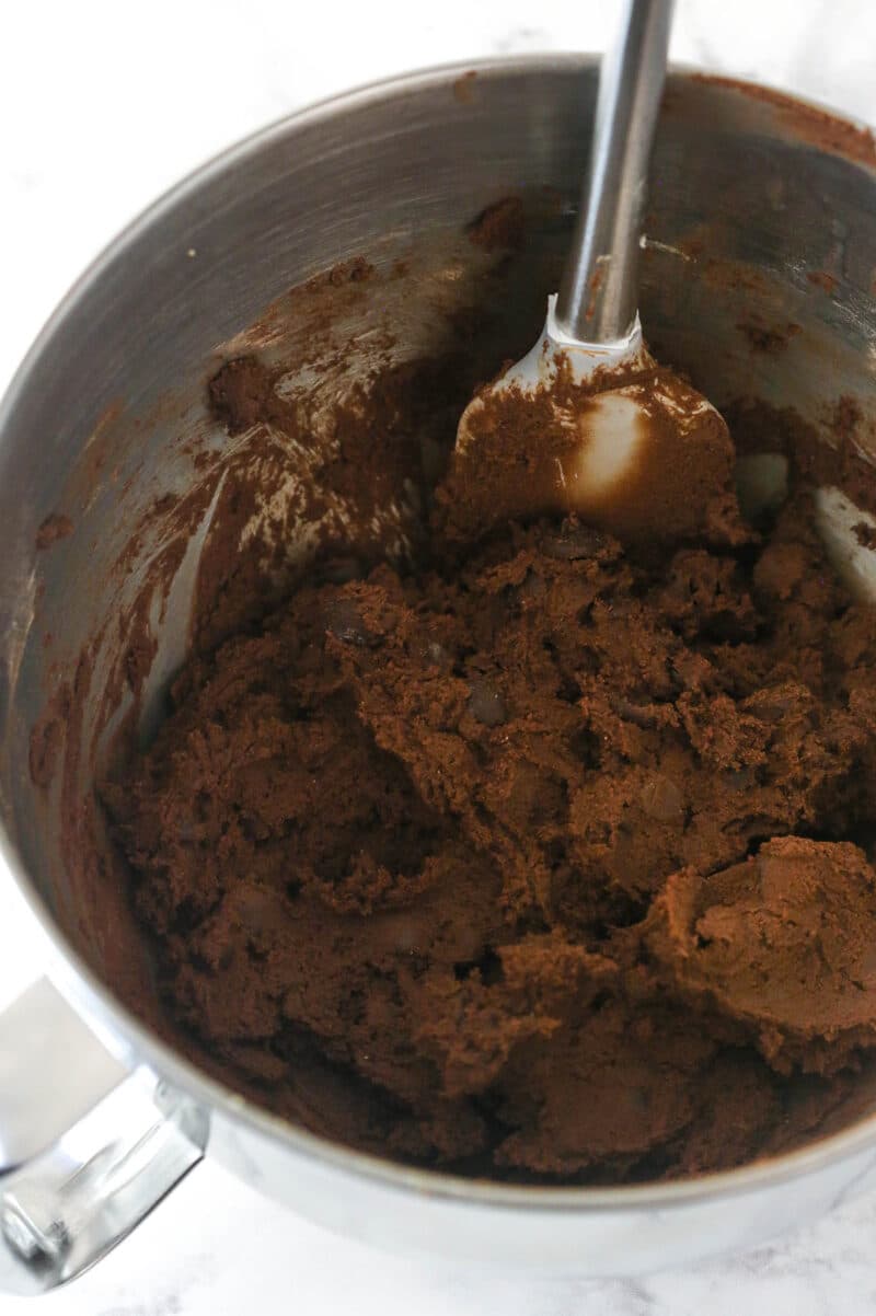 Triple chocolate cookie cake is made up of a fudgy chocolate cookie base loaded with chocolate chips and topped with chocolate buttercream. Combining wet and dry ingredients for chocolate cookie cake and mixing in chocolate chips.