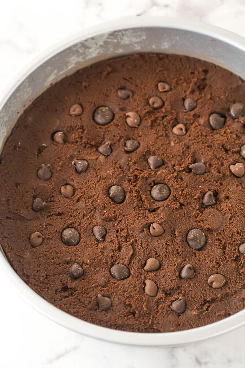 Chocolate cookie dough in a cake pan sprinkled with chocolate chips.