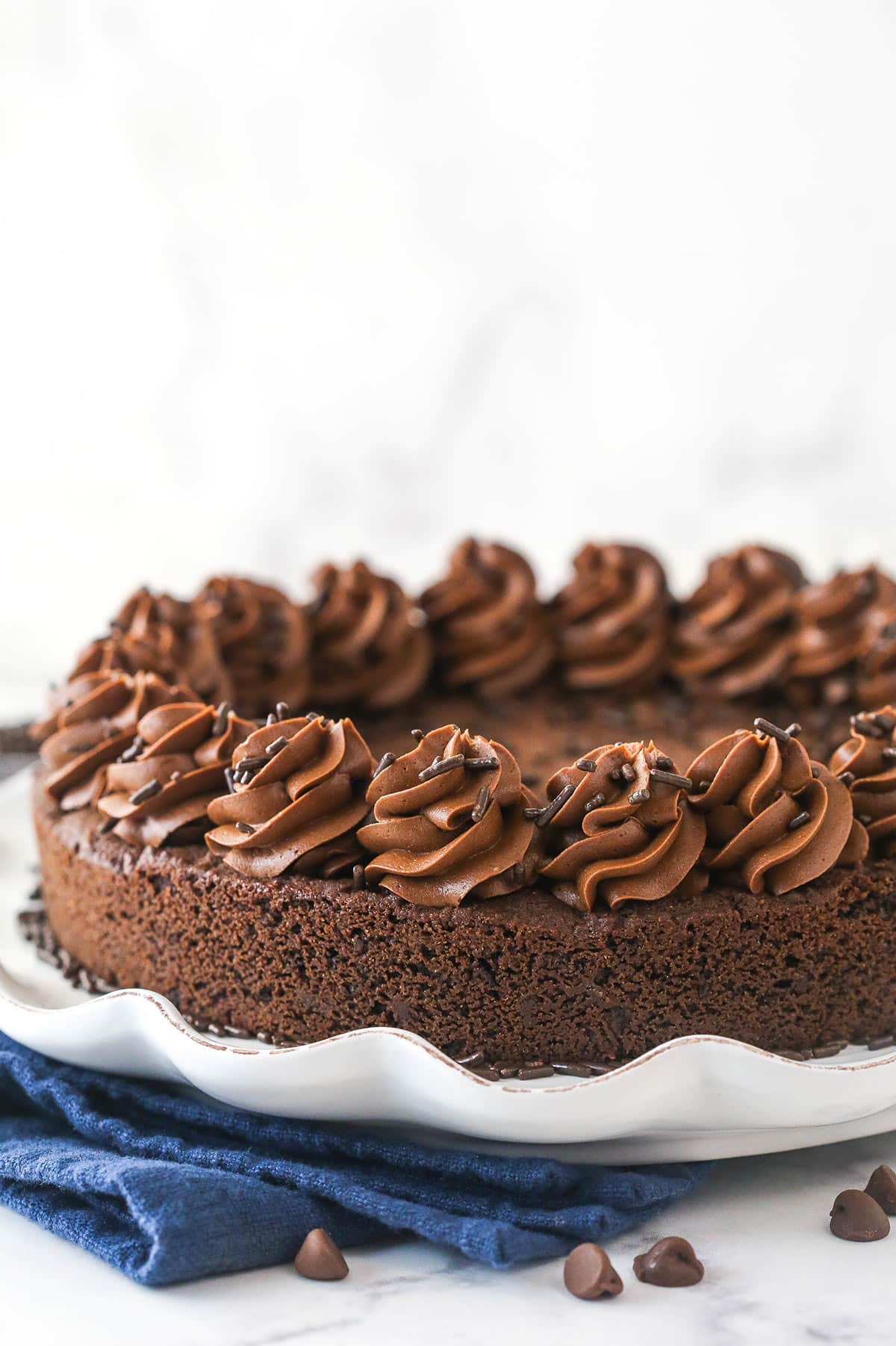 Triple chocolate cookie cake is made up of a fudgy chocolate cookie base loaded with chocolate chips and topped with chocolate buttercream. Chocolate cookie cake on a serving platter.