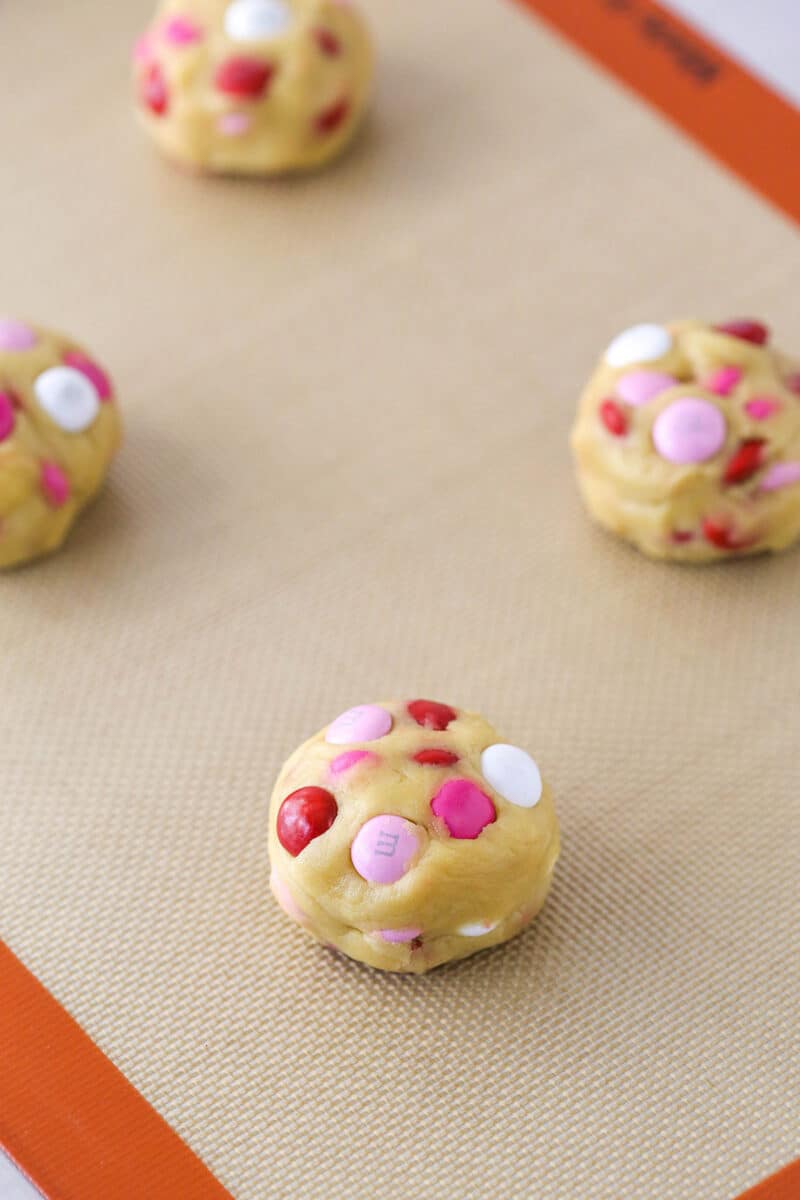 Valentine's Day M&M cookie dough formed into balls and arranged on a silicone baking mat.