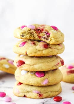 A stack of Valentine's Day M&M cookies. The top cookie has a bite taken out of it.