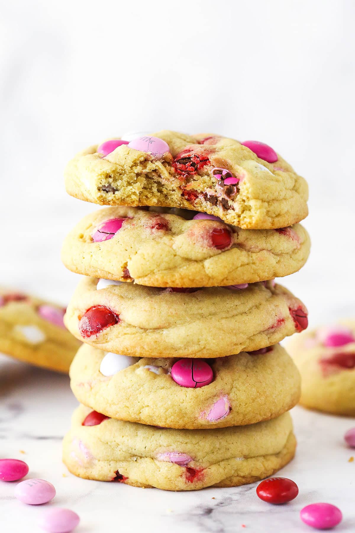 A stack of Valentine's Day M&M cookies. The top cookie has a bite taken out of it.