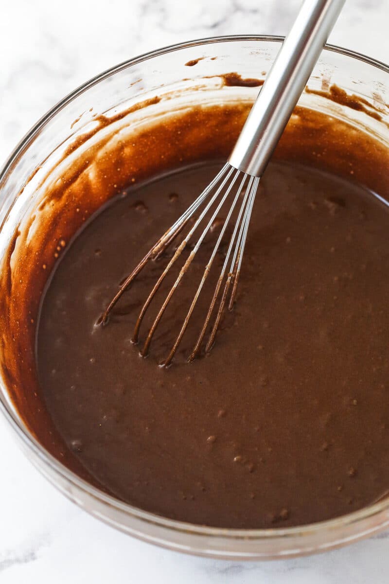 Whisking flour and cocoa powder into the wet ingredients for brownie batter.