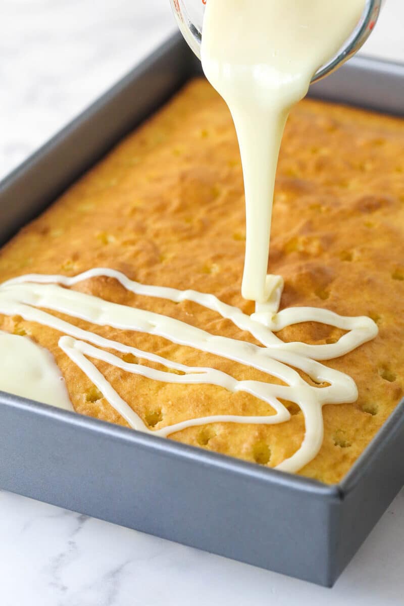 Pouring sweetened condensed milk over a yellow cake with holes poked in it.