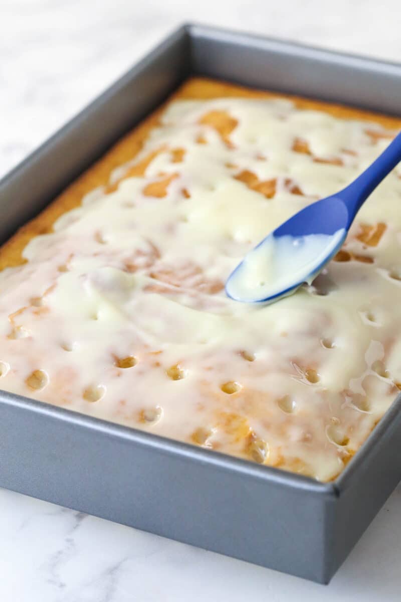 Spreading sweetened condensed milk over a yellow cake with holes poked in it.