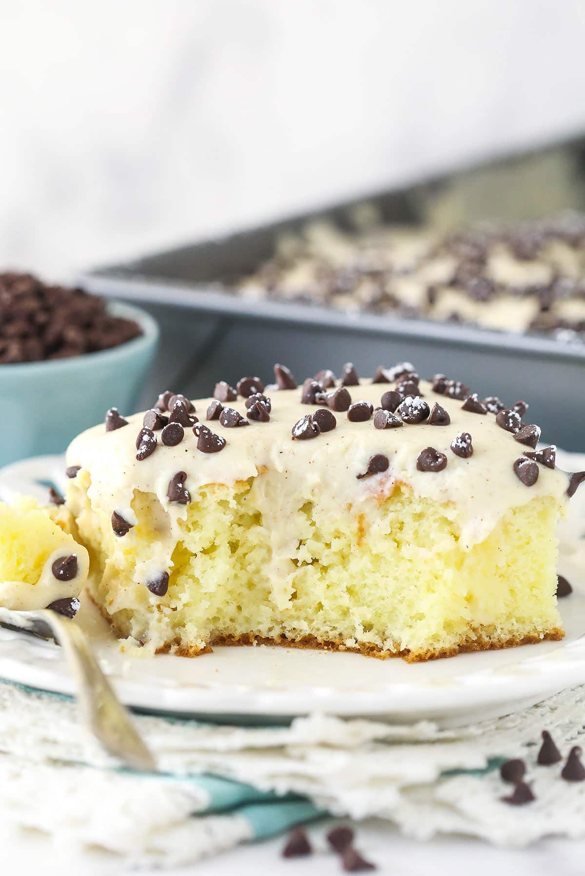 A slice of cannoli poke cake with a bite taken out of it served on a plate.