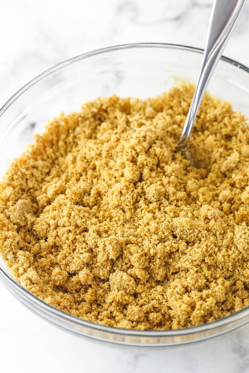 Mixing together graham cracker crumbs, melted butter, and sugar to make a graham cracker crust.