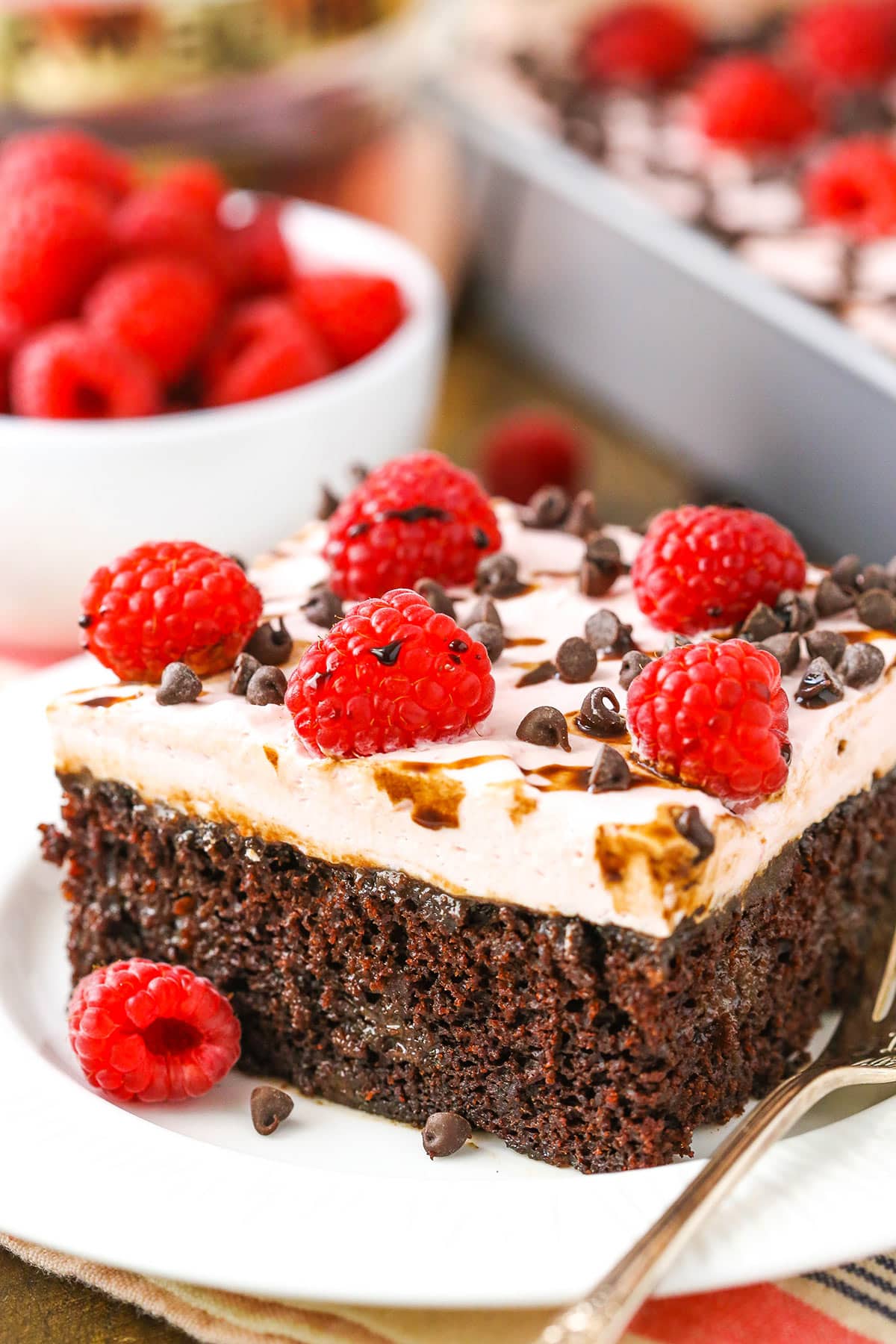 A square serving of Raspberry Chambord Chocolate Poke Cake next to a silver fork on a white plate