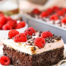 A square serving of Raspberry Chambord Chocolate Poke Cake next to a silver fork on a white plate