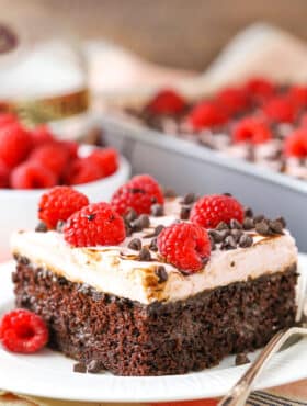 A square serving of Raspberry Chambord Chocolate Poke Cake next to a silver fork on a white plate