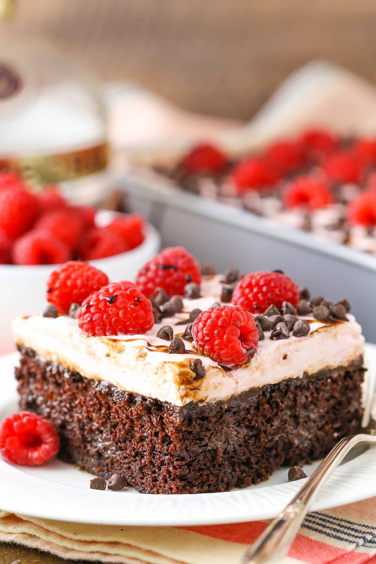 A square serving of Raspberry Chambord Chocolate Poke Cake next to a silver fork on a white plate