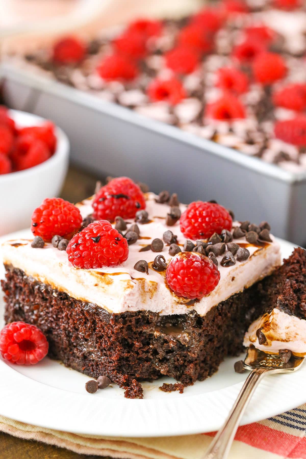 A square serving of Raspberry Chambord Chocolate Poke Cake missing a bite next to a silver fork on a white plate