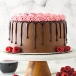 Red wine chocolate cake on a cake stand near a bowl of raspberries.