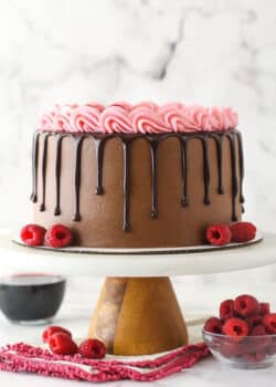 Red wine chocolate cake on a cake stand near a bowl of raspberries.