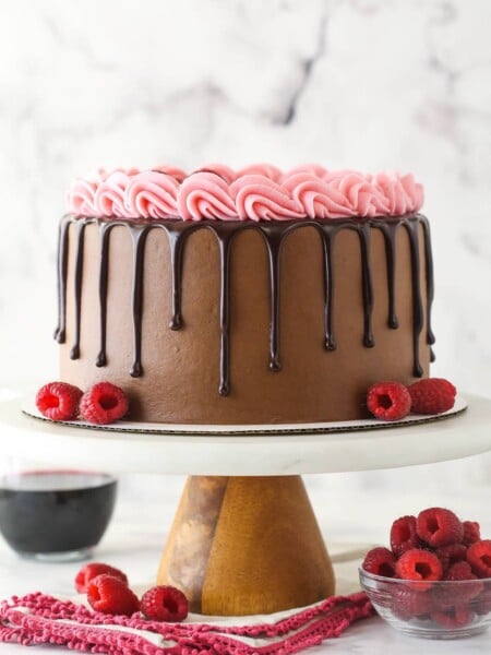 Red wine chocolate cake on a cake stand near a bowl of raspberries.