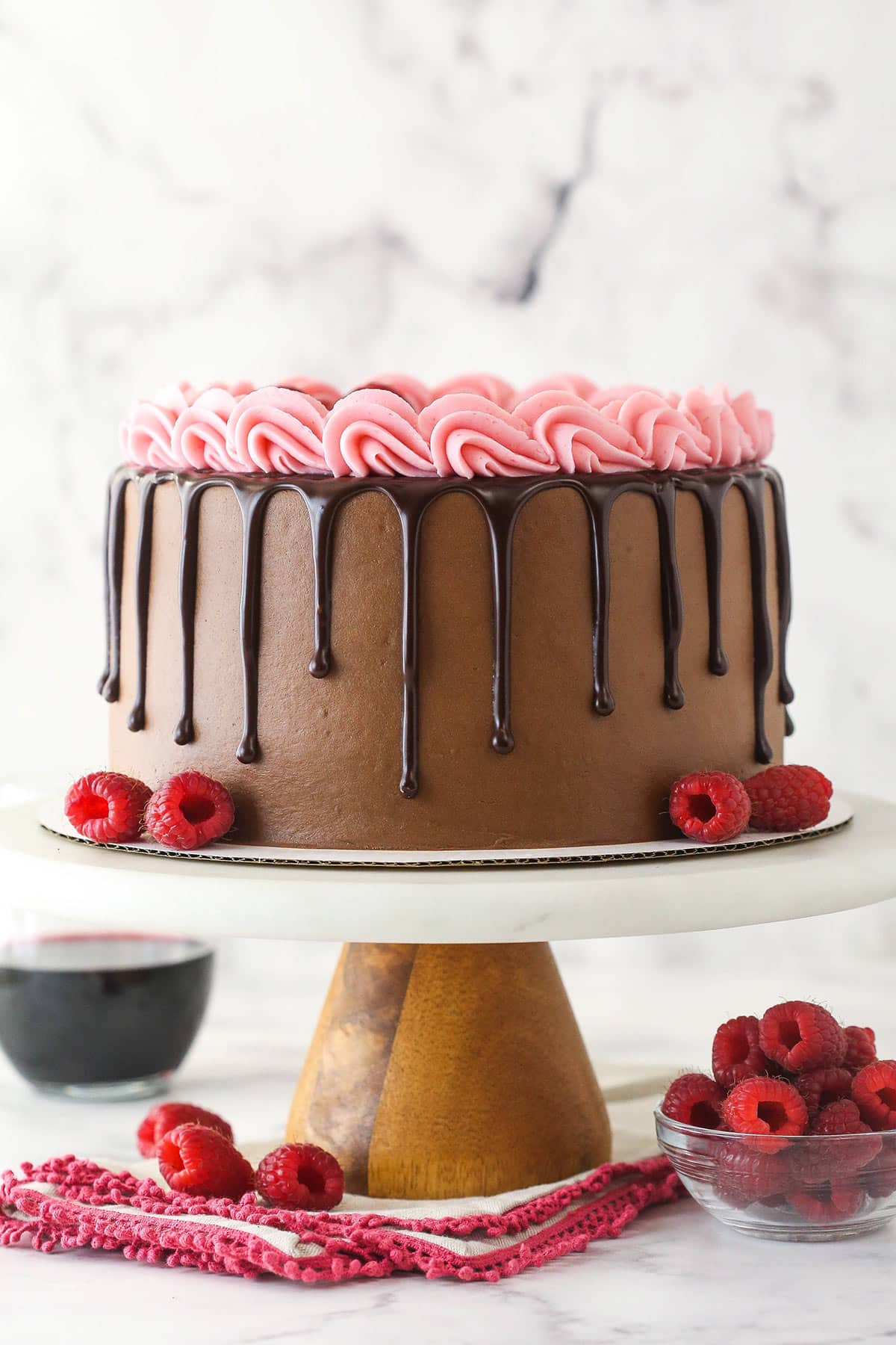Red wine chocolate cake on a cake stand near a bowl of raspberries.
