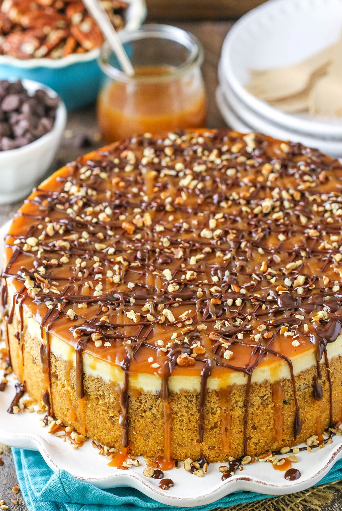 This Turtle Cheesecake Recipe is made with a graham cracker crust and plenty of caramel, chocolate and pecans! It's rich, creamy and sure to be a hit! Overhead view of Turtle Cheesecake on a white platter