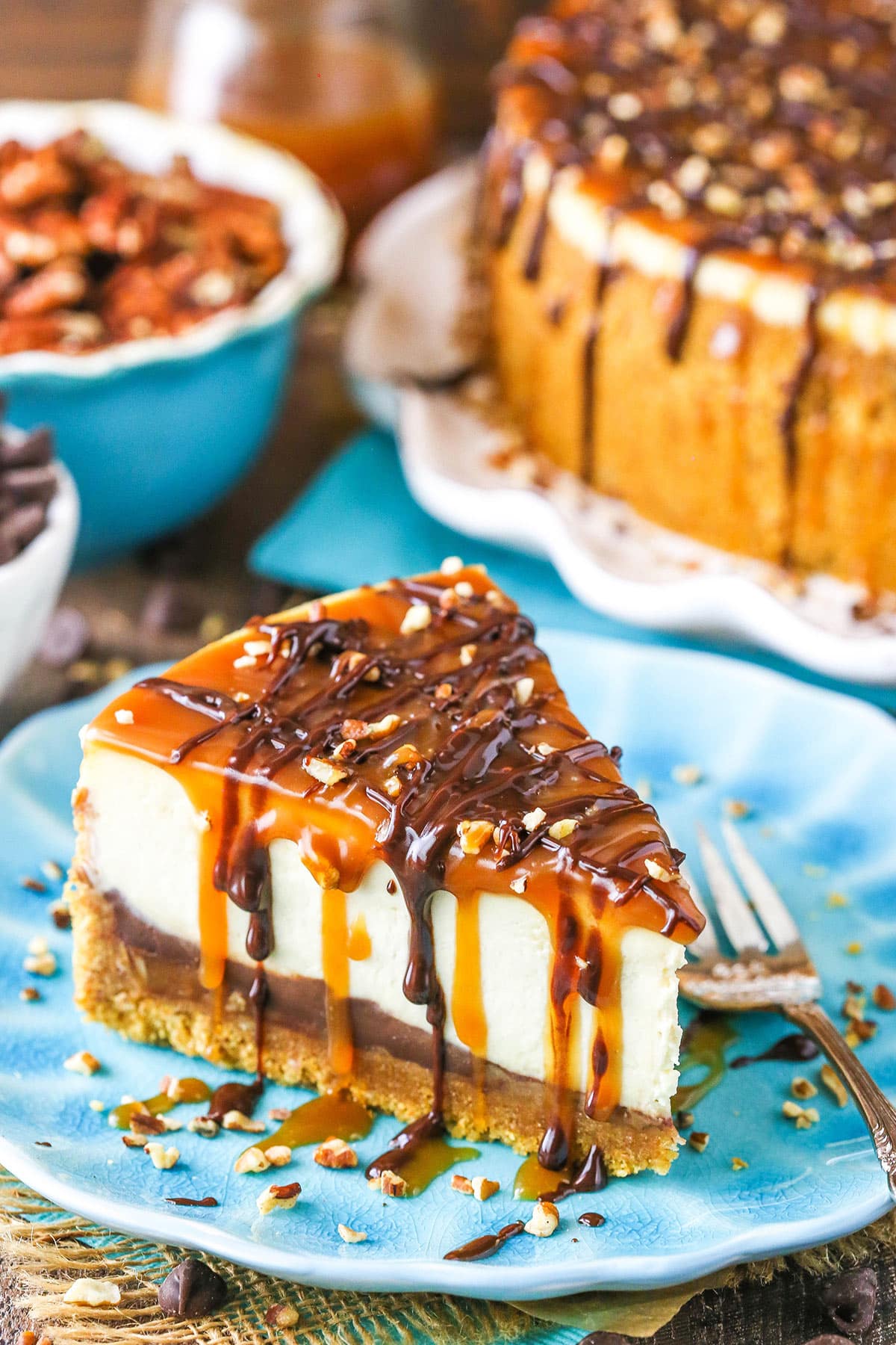 A slice of Turtle Cheesecake next to a fork on a blue plate