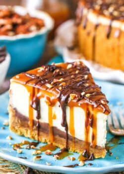 A slice of Turtle Cheesecake next to a fork on a blue plate