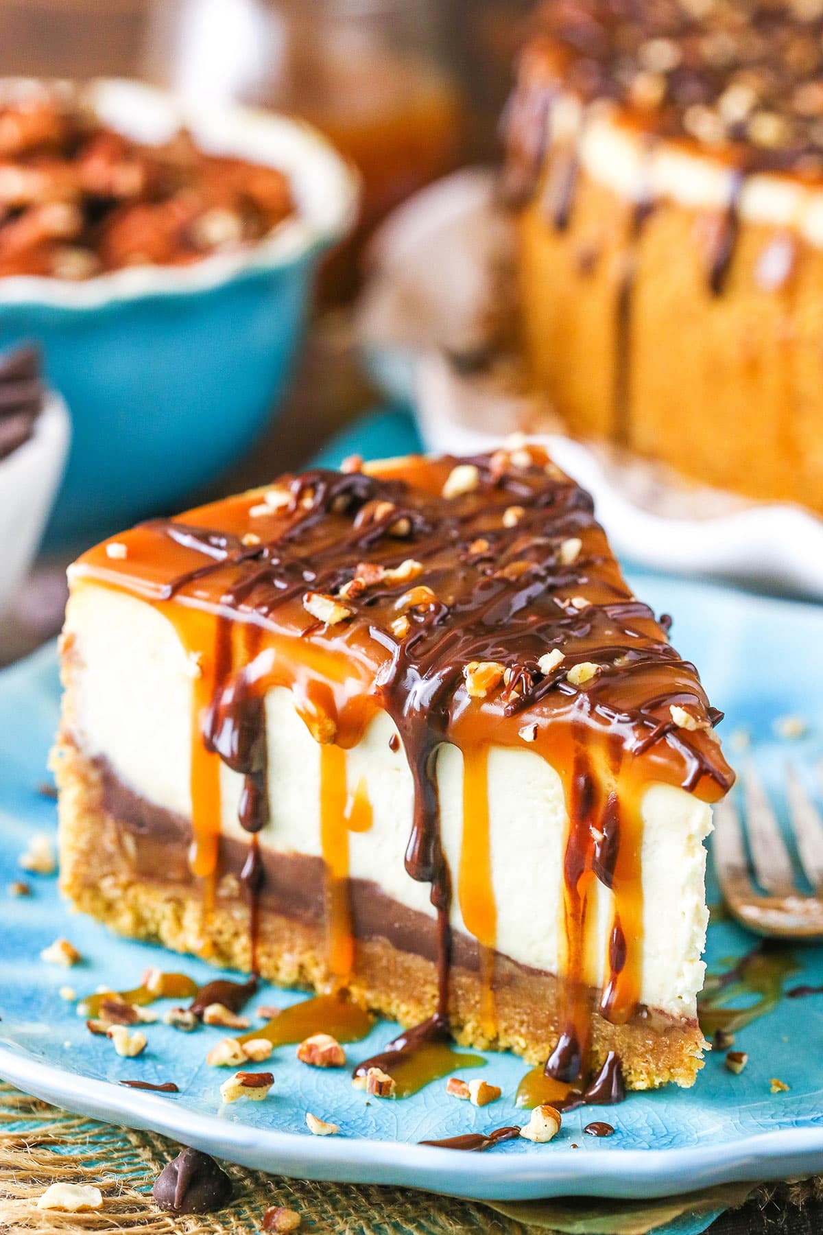 A slice of Turtle Cheesecake next to a fork on a blue plate