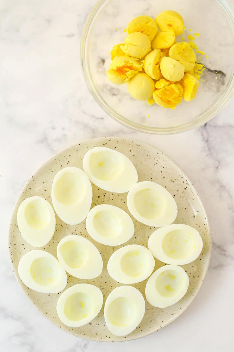 Hard boiled egg yolks in a bowl next to a plate of hollowed out hard boiled egg whites.