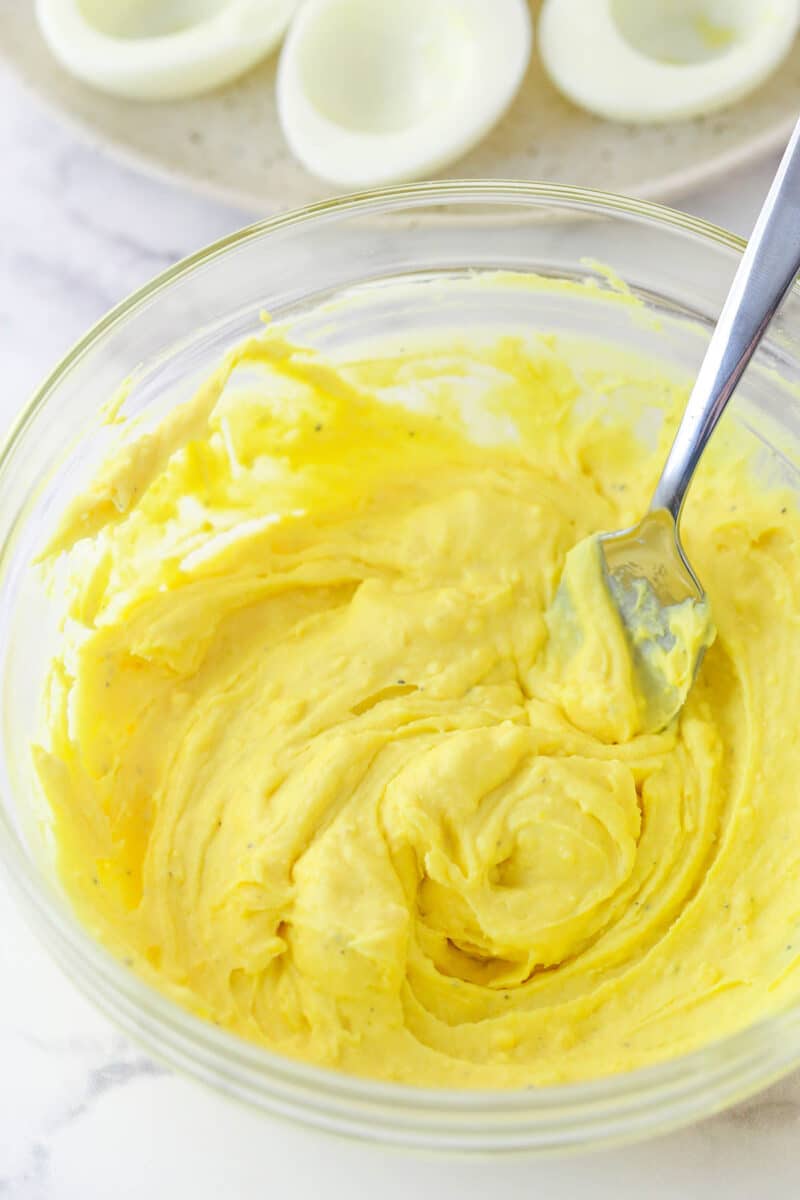 Mixing together mayo, mustard, salt, and pepper to mashed egg yolks.