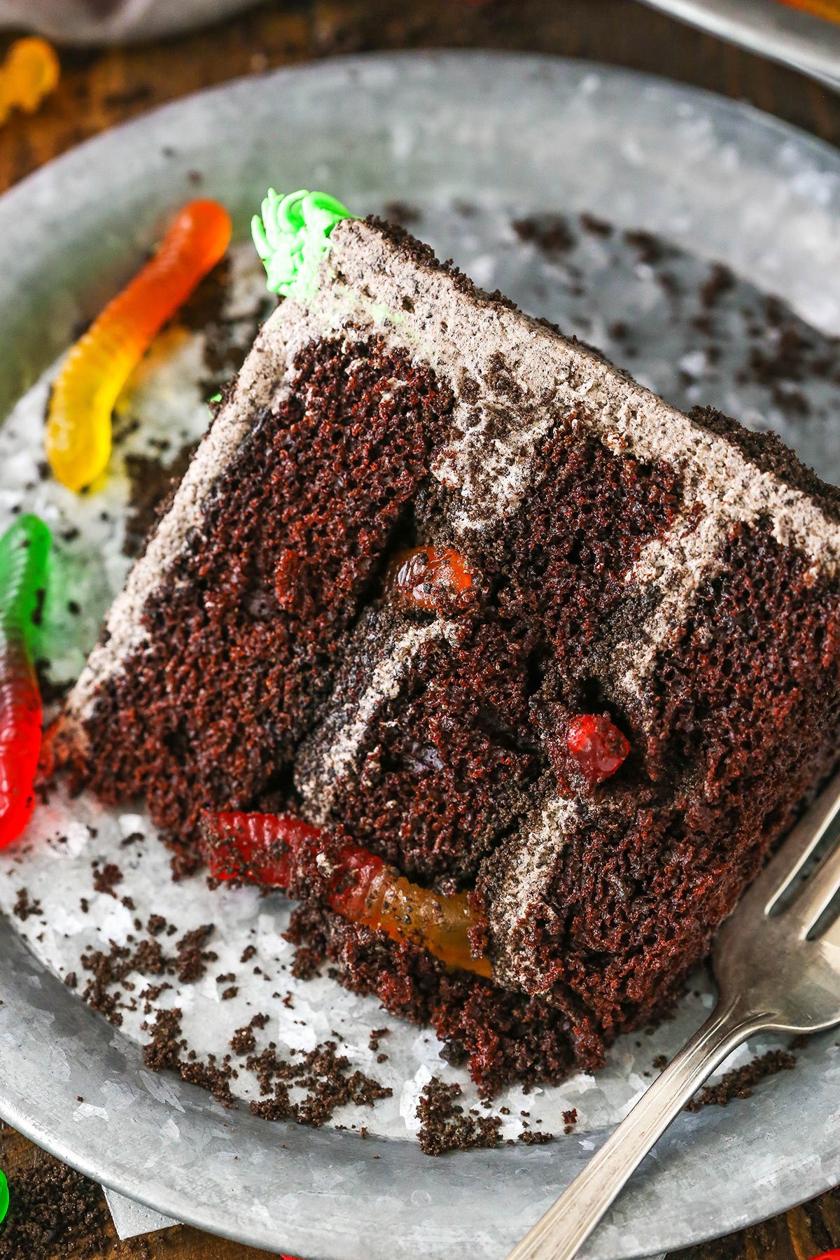 This Dirt Cake is a moist chocolate cake filled with frosting that's loaded with Oreos and layered with more Oreo crumbs! A slice of Dirt Cake next to a silver fork on a gray plate