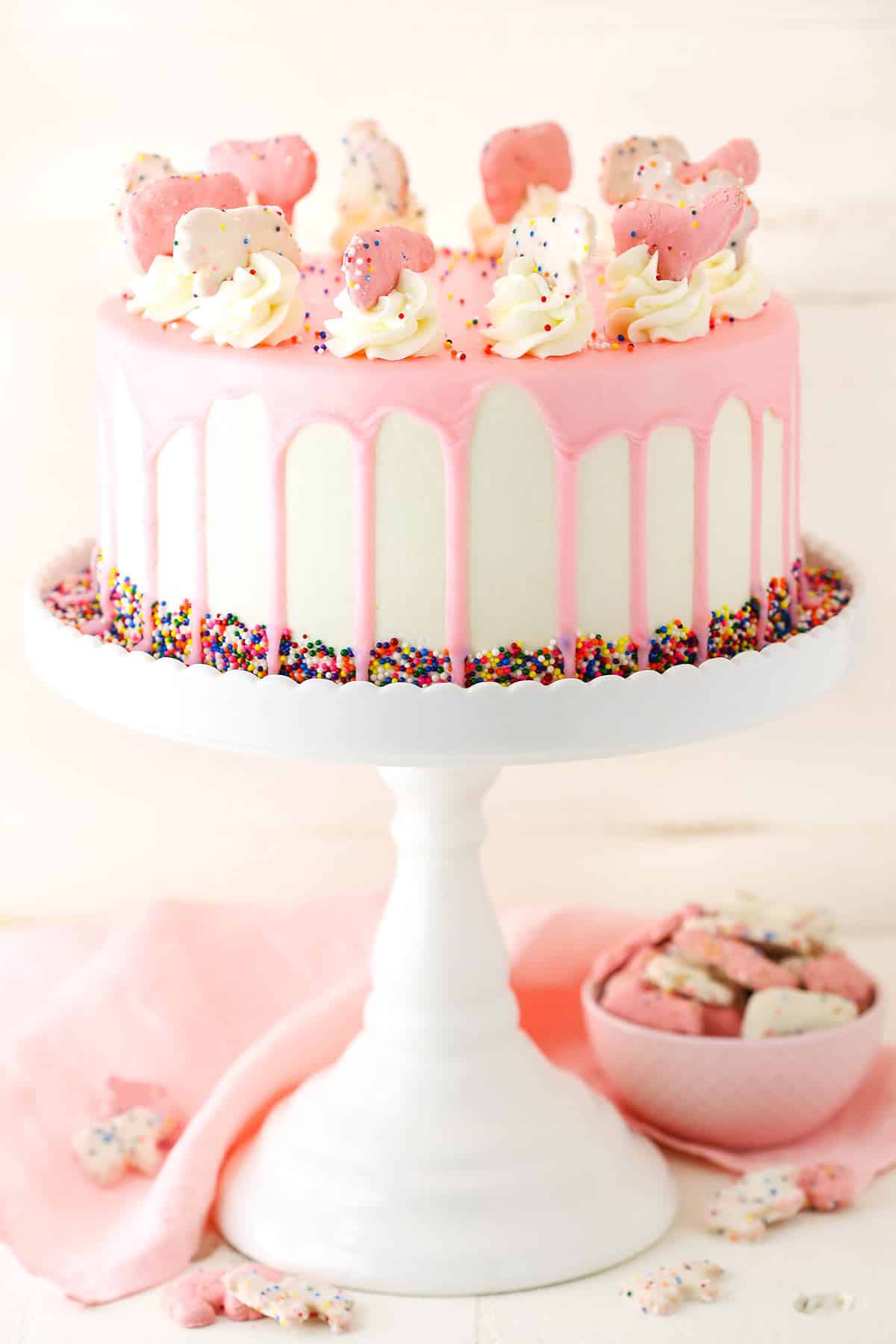 Side view of a full Frosted Circus Animal Cookie Cake on a white cake stand