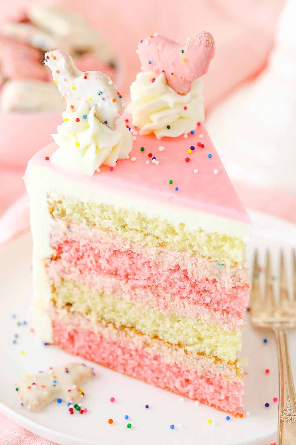 A slice of Frosted Circus Animal Cookie Cake next to a silver fork on a white plate