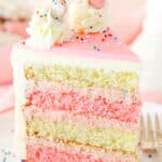 A slice of Frosted Circus Animal Cookie Cake next to a silver fork on a white plate