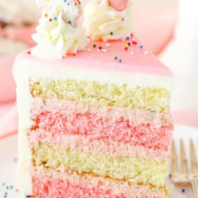 A slice of Frosted Circus Animal Cookie Cake next to a silver fork on a white plate