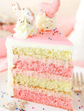 A slice of Frosted Circus Animal Cookie Cake next to a silver fork on a white plate