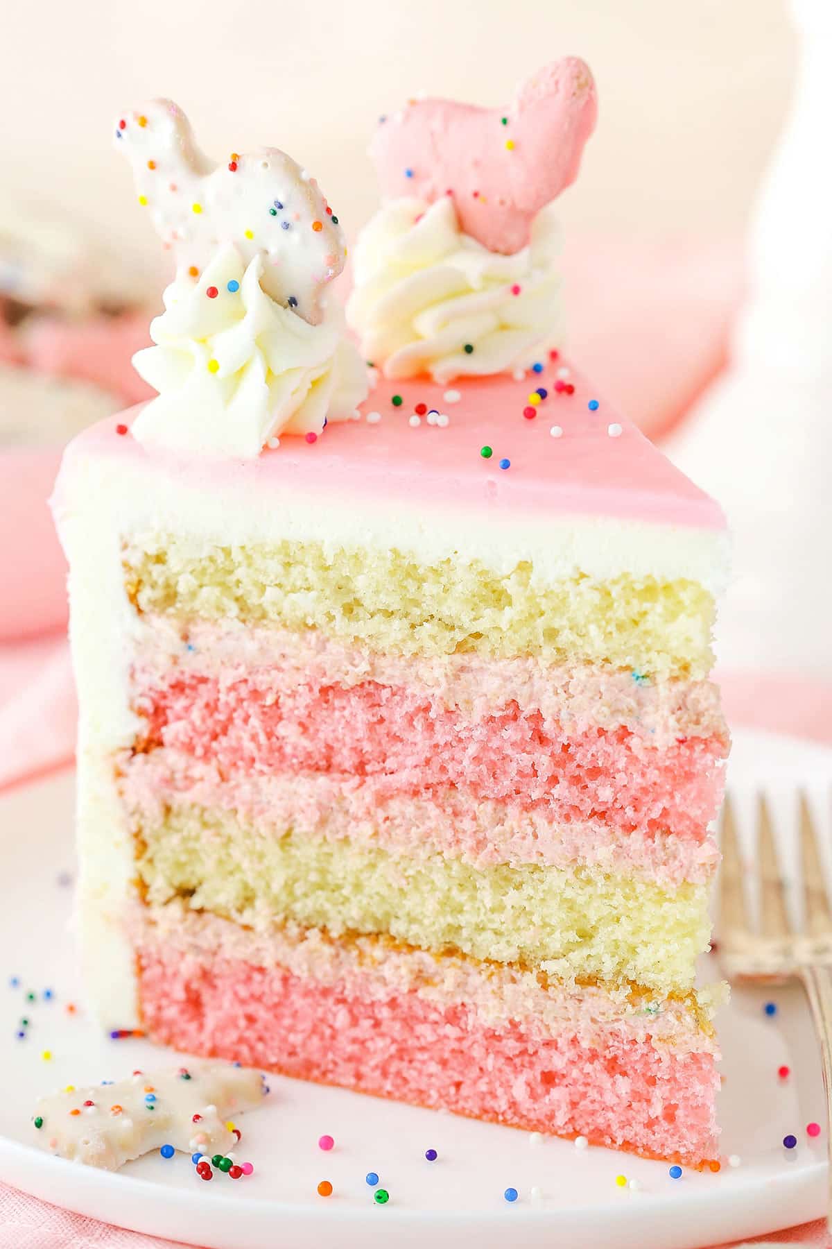 A slice of Frosted Circus Animal Cookie Cake next to a silver fork on a white plate