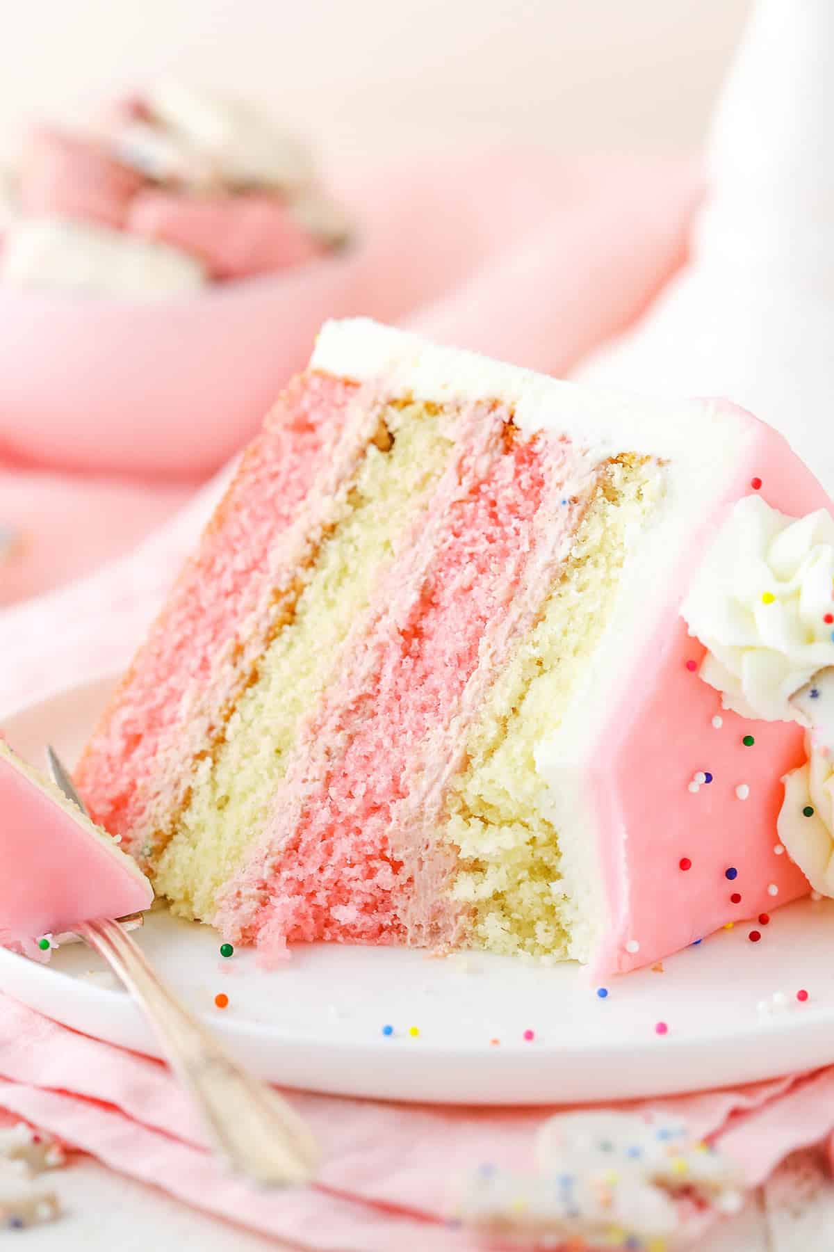 A slice of Frosted Circus Animal Cookie Cake on it's side next to a silver fork on a white plate