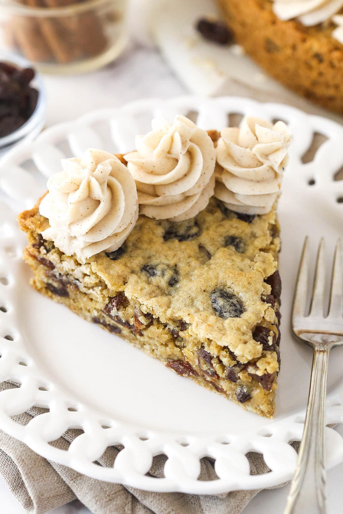 Oatmeal raisin cookie cake is soft and chewy, loaded with warming cinnamon and sweet raisins, and topped with the best maple buttercream. Overhead image of a slice of oatmeal raisin cookie cake on a plate with a fork.