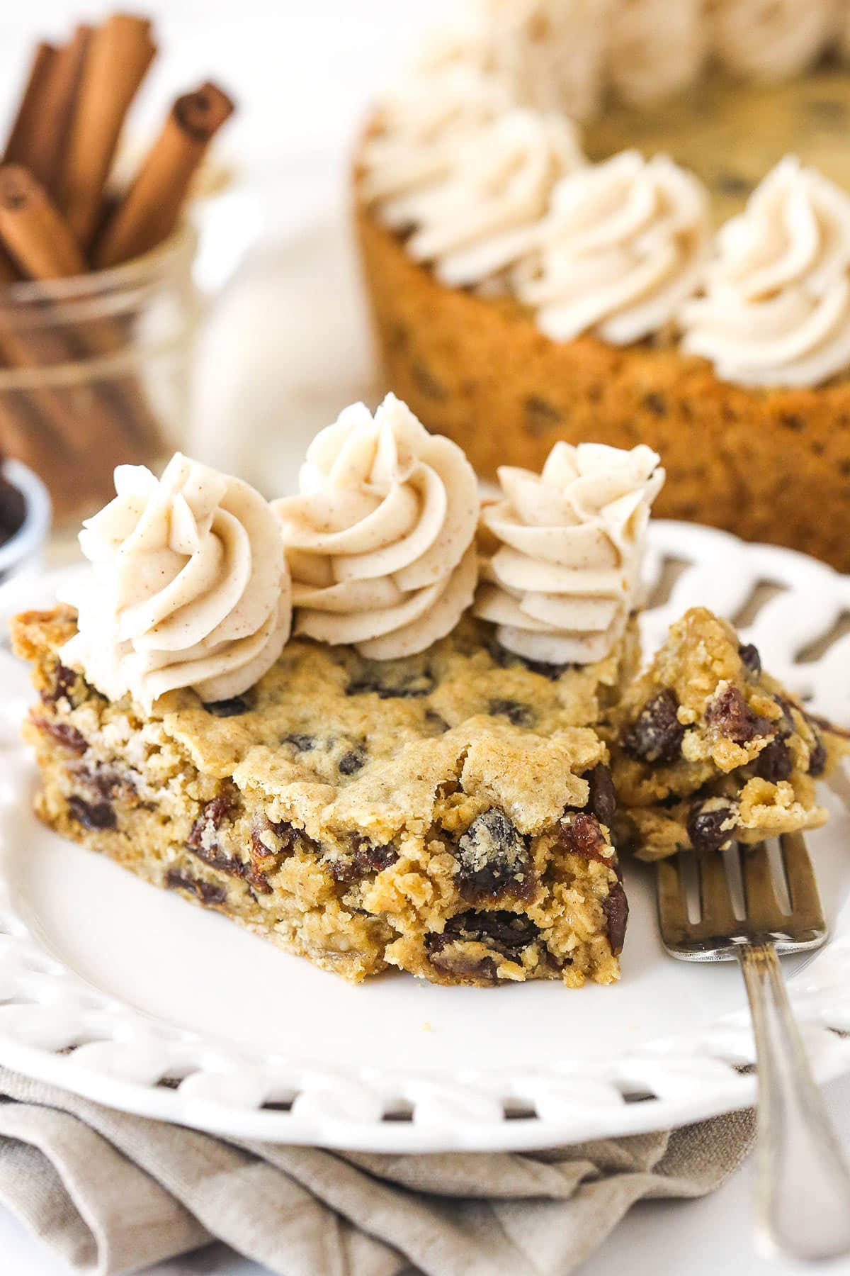 Oatmeal raisin cookie cake is soft and chewy, loaded with warming cinnamon and sweet raisins, and topped with the best maple buttercream. A fork taking a bite out of a slice of oatmeal raisin cookie cake.