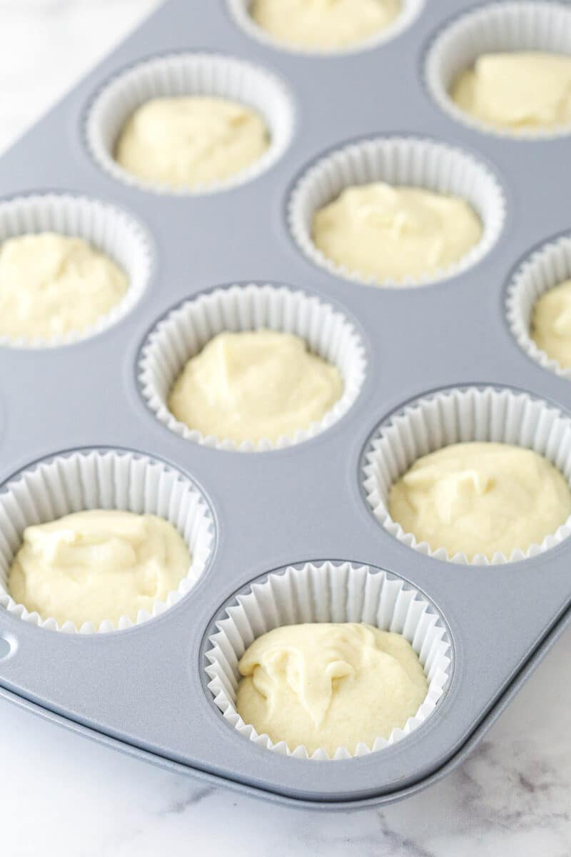 Filling cupcake liners in a cupcake tin with vanilla cupcake batter.