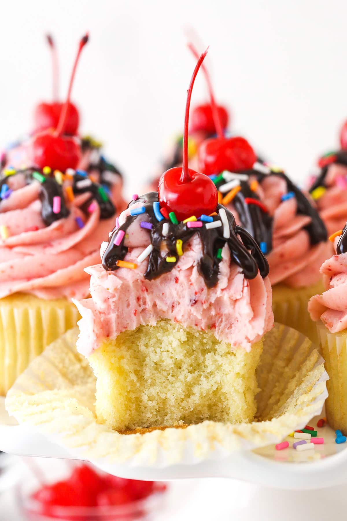 A strawberry sundae cupcake with a bite taken out of it.