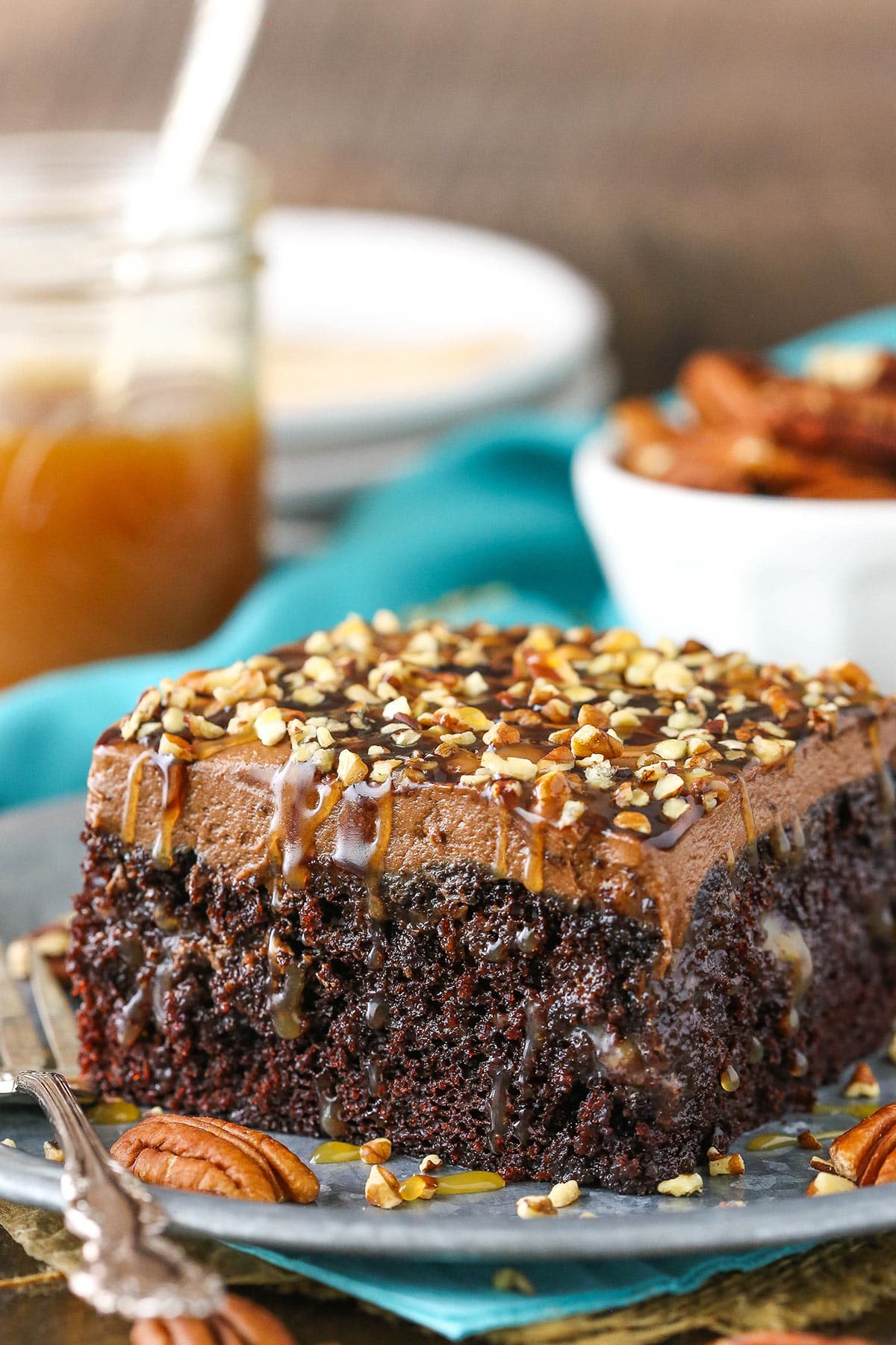 A square serving of Chocolate Turtle Poke Cake next to a silver fork on a gray plate