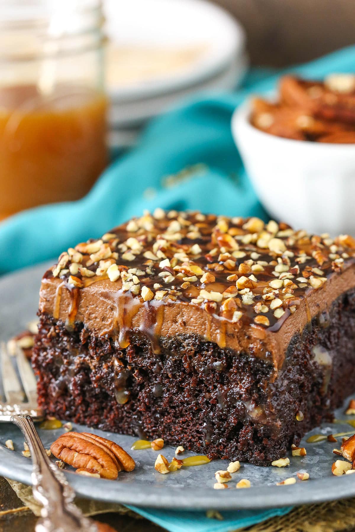 A square serving of Chocolate Turtle Poke Cake next to a silver fork on a gray plate