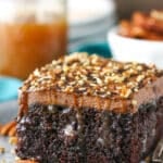 A square serving of Chocolate Turtle Poke Cake next to a silver fork on a gray plate