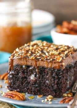 A square serving of Chocolate Turtle Poke Cake next to a silver fork on a gray plate